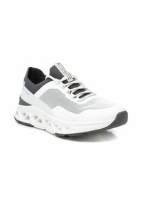 Zapatilla deportiva blanca con parte superior texturizada, acentos grises, suela flexible con recortes circulares y puntera negra en contraste.