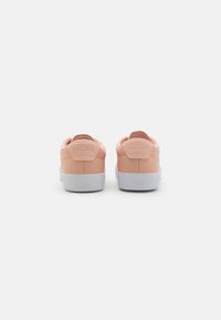 Baskets en cuir synthétique rose avec semelles en caoutchouc blanc, dotées d'une bande de talon et du logo Lacoste embossé à l'arrière.