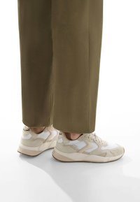 Sneaker beige e bianche con una parte superiore testurizzata, punta rotonda e suola ammortizzata, abbinate a pantaloni a gamba larga verde oliva.