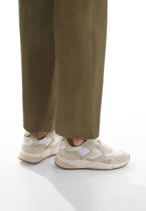 Sneaker beige e bianche con una parte superiore testurizzata, punta rotonda e suola ammortizzata, abbinate a pantaloni a gamba larga verde oliva.
