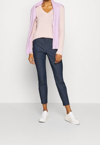 Suéter de punto rosa claro con escote en V, superpuesto con un cárdigan lavanda; combinado con pantalones oscuros ajustados y zapatillas de plataforma blancas.