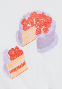 Γραφικό κέικ με ροζ γλάσο και φράουλες στην κορυφή, δίπλα μια φέτα που αποκαλύπτει στρώσεις, με ετικέτα «ABERCROMBIE» σε κίτρινο φόντο.