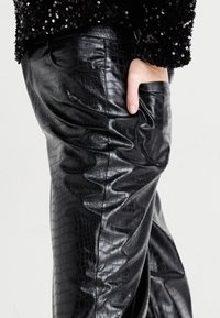 Pantalons en faux cuir noir avec un motif crocodile texturé, à coupe ajustée et poche latérale. Le tissu a un léger éclat.