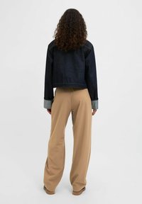 Donkerdenim cropped jack met lichtdenim manchetten, gecombineerd met hooggesneden, wijdvallende beige broeken. Soepele texturen en een getailleerde pasvorm.