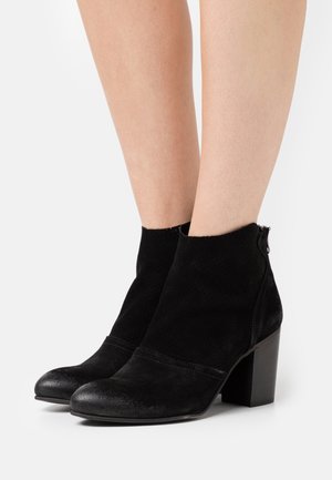 Bottines noires en suede, avec un bout lisse et un upper texturé. Talon carré et fermeture à glissière sur le côté.