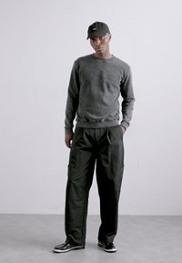 Felpa grigia in tessuto texturizzato, abbinata a pantaloni neri larghi. Un berretto scuro e scarpe nere completano il look informale. Design semplice in tutto.