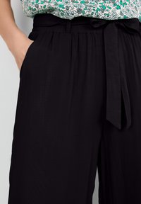 Pantalones anchos negros con una cinturilla alta, que cuentan con un cinturón de lazo. Textura suave y bolsillos laterales. Combinados con una blusa de estampado floral.