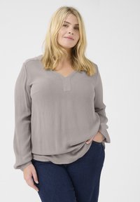 Blouse grise à manches longues avec un d�écolleté en V, en tissu doux et texturé, au fit décontracté, associée à un jean bleu foncé.