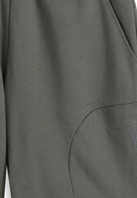 Pantalones jogger de tela suave de color verde oscuro con un ajuste relajado, que cuentan con un bolsillo lateral y un detalle sutil del logo. Textura lisa y diseño casual.