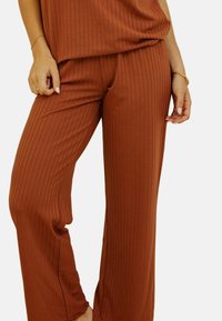 Pantalons à jambes larges et côtelés dans une couleur rouille. Texture de tissu douce avec une coupe décontractée, dotés d'une taille haute et sans fermetures visibles.