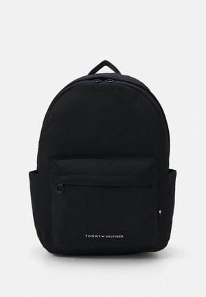 Black backpack made of durable fabric, featuring a rounded shape, front pocket, and small logo at the bottom. Includes a top handle.