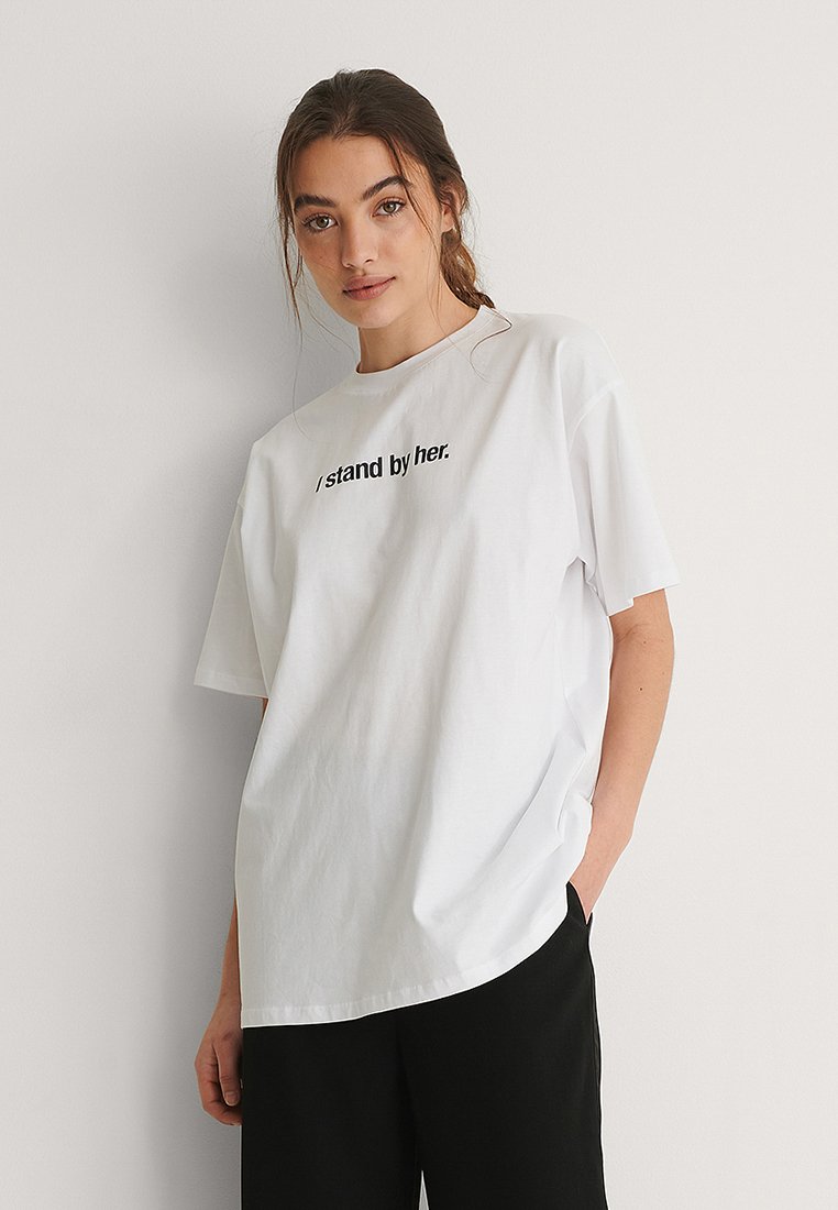T-shirt en coton blanc à manches courtes, avec un texte imprimé noir "Je la soutiens." Coupe décontractée avec un col rond et une texture douce.
