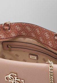 Borsa beige con esterno liscio e hardware dorato. L'interno presenta una fodera a motivi rosa e una tasca con zipper. Logo visibile.