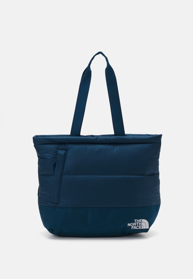 Sac fourre-tout matelassé bleu marine avec deux sangles d'épaule et une poche latérale zippée, marqué du logo The North Face dans le coin inférieur.