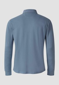 Lange mouwen poloshirt van zachte blauwe stof, met een klassieke kraag, rechte zoom en zonder zichtbare logo's of patronen. Zachte textuur, minimaal ontwerp.