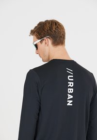 Zwarte lange mouwen shirt met een textuurafwerking, met een verticale witte print die "//URBAN" op de achterkant leest.
