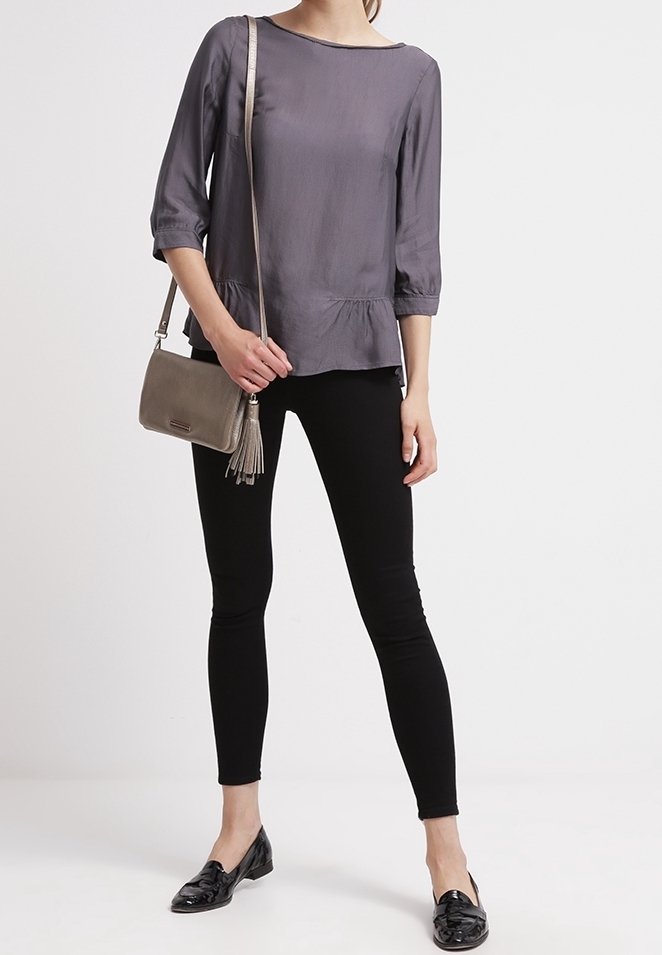 Harmaa peplum-pusero, jossa on kolme neljännesosaa hihat, yhdistetty mustiin slim fit -farkkuihin ja mustiin loafer-kenkiin. Harmaa käsilaukku, jossa on tupsuelementti.