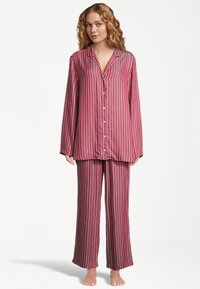 Randig pyjamaset i vinröd och vit, med en knäppning framtill och långärmad topp samt löst sittande byxor. Mjuk, slät tyg med vida benöppningar.