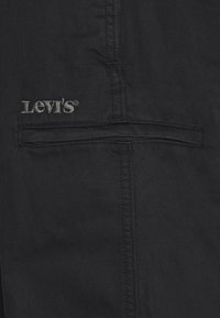 Svart denimtyg med en texturerad yta, försett med en stickad ficka och en grå "Levi's"-logotyp broderad ovanför fickan.
