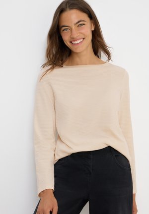 Haut beige clair à manches longues avec des rayures horizontales et un col bateau, associé à un pantalon noir comportant des poches latérales. Texture douce.