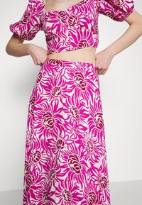 Un crop top floral rose à manches courtes bouffantes et détails de boutons, associé à une jupe longue et fluide dans un motif floral assorti.