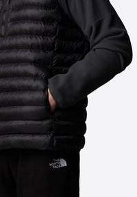 Zwarte gewatteerde vest met horizontale baffles, gecombineerd met een zwart fleece shirt. Voorzien van elastische manchetten en zijzakken. Subtiel logo op het fleece.