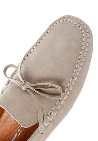 Hellbeige Wildleder-Mokassinschuhe mit runder Zehenform, genähten Akzenten und einer Schleife an der Vorderseite. Das Innere besteht aus braunem Leder.