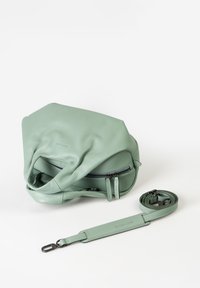 Groene leren tas met textuur, voorzien van een ritssluiting, twee ritstoetsen en een verstelbare schouderband ernaast geplaatst.