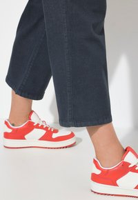 Zapatillas deportivas rojas y blancas con paneles texturizados y una gruesa suela de goma blanca. Combinadas con pantalones cropped de mezclilla oscura.