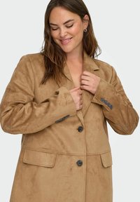 Brauner Wildledermantel mit Reverskragen, Ein-Knopf-Verschluss und vorderen Taschen. Verfügt über eine weiche Textur und schwarze Knöpfe an den Ärmeln.