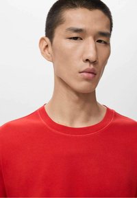 Červené bavlnené tričko s okrúhlym výstrihom a krátkymi rukávmi, s hladkou textúrou a minimalistickým dizajnom. Čistá, jednofarebná farba.