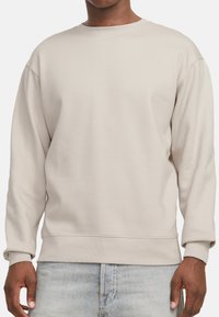 Beige sweater met ronde hals gemaakt van zachte stof, met verlaagde schouders en geribbelde manchetten, gecombineerd met lichte blauwe denim shorts.