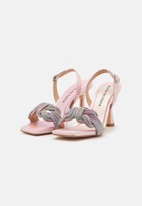 Růžové sandály na vysokém podpatku s pleteným korálkovým páskem, čtvercovou špičkou a štíhlým páskem kolem kotníku se kovovou přezkou.