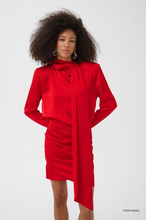 Woman with voluminous hair wearing a long-sleeve, ruched red dress with an asymmetrical draped scarf detail.