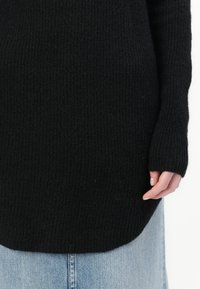 Maglione nero a coste con maniche lunghe e orlo curvo verso l'alto, abbinato a denim blu chiaro. Tessuto testurizzato, vestibilità morbida.