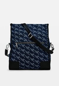 Borsa in denim blu con motivo floreale, dettagli neri, tracolla regolabile e tasca frontale con zip. Forma rettangolare con texture morbida.