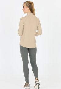 Beige top met lange mouwen en een hoge hals, gecombineerd met groene leggings. De top heeft een gladde textuur en een aansluitend ontwerp.
