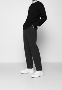 Black ribbed sweater, gray pants with side pockets, and white sneakers, standing pose against a plain white background.