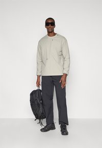 Haut à manches longues gris clair, pantalon cargo noir et sac à dos noir. Les lunettes de soleil et les chaussures ont un design élégant et fonctionnel.