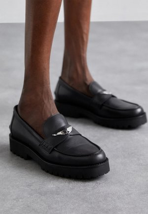 Schwarze Lederloafers mit runder Zehe, mit einem silbernen Akzent am Riemen und einer dicken, strukturierten Sohle für zusätzlichen Grip.