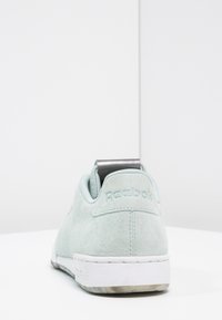 Mintgröna mockasneakers med kontrasterande grå hälflik och vit gummisula med texturerade detaljer. "Reebok"-logotyp präglad.