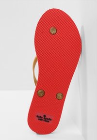 Röd gummijobb med en strukturerad yta, guldfärgade detaljer nära mitten, och en logotyp som säger "kate spade NEW YORK" vid hälen.