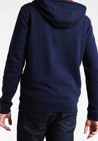 Mörkblå hoodie med mjuk textur, framficka i kangaroo-stil, justerbar dragsko på huvan och ribbade ärmslut och nederkant.