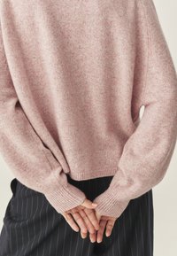 Jasnoróżowy sweter dziany o luźnym kroju, z prążkowanymi mankietami i dołem. Miękka faktura, opuszczone szwy ramion i minimalne detale wzornicze.