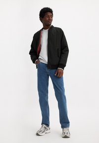 Chaqueta bomber negra con forro rojo, sudadera gris, jeans azules y zapatillas grises. Tejido suave y corte relajado.
