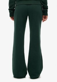 Pantalones de chándal acampanados de color verde oscuro, hechos de tela suave, con una textura lisa y un diseño de pierna ancha. Sin marcas visibles ni bolsillos.