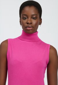 Sømløs mock turtleneck top i lys pink strikstof. Har en ribbet halskant og en glat tekstur. Minimalistisk design uden yderligere detaljer.