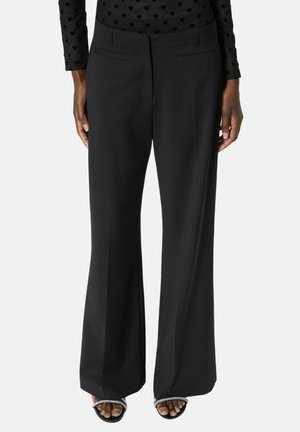 Vrouw draagt zwarte broek met wijde pijpen en open sandalen met strassbandjes, gecombineerd met een zwarte top met lange mouwen en hartpatronen.