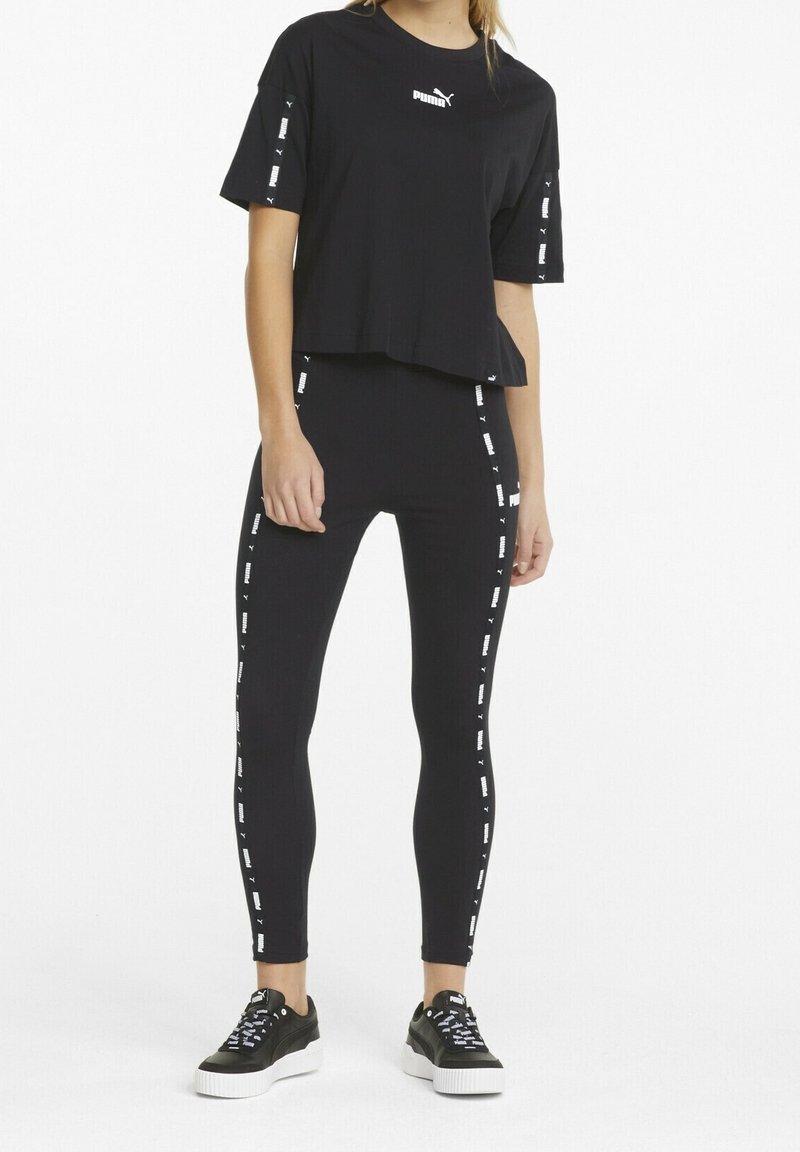 Black cropped t-shirt and leggings set, featuring white branded accents on sleeves and sides, paired with black sneakers with white soles.