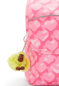 Sac à dos rose avec motif camouflage ; présente une chaîne avec un porte-clés en peluche de singe jaune et un détail de visage brun. Accent de fermeture éclair argenté.